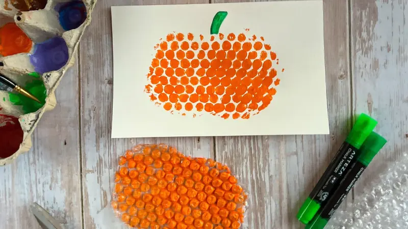 Toddler doing bubble wrap printing craft activity with colorful paint on white paper