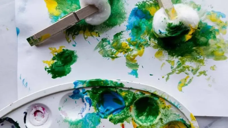 Toddler dabbing cotton ball in colorful pastel paint to create dot art on paper – easy cotton ball painting craft for kids